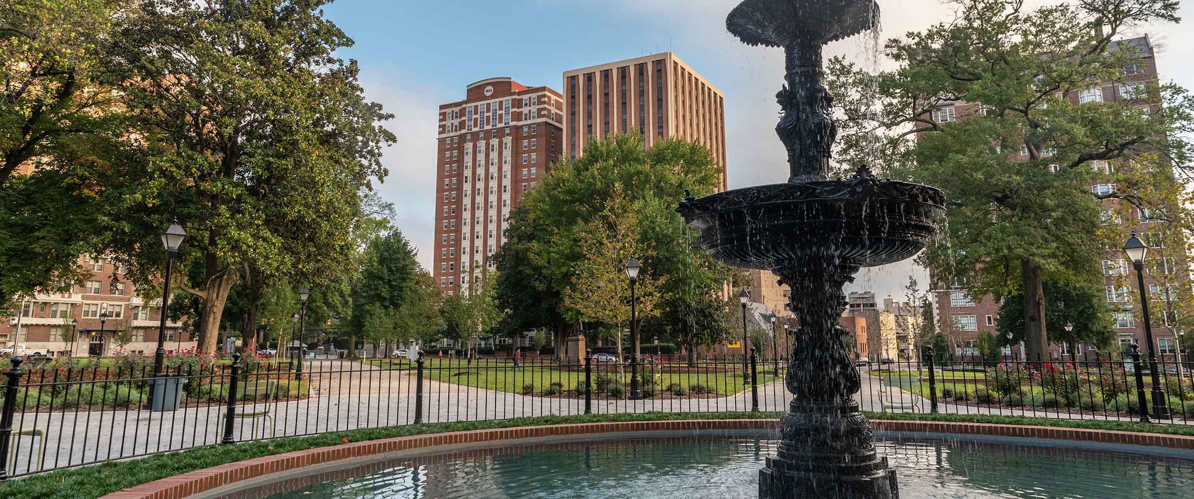 A fountain in Monroe Park with Brandt Hall and Rhoads Hall in the background